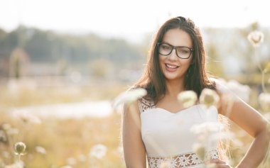 Çayırda çimenlerde poz veren güzel, genç bir kadın ve dışarıda kameraya bakıyor. Yarım boy. Olumlu duyguları olan güzel bir kadın, gülen surat. 30 'lu yaşlardaki kadın