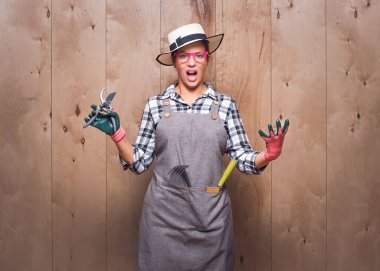 Kızgın kadın çiftçi kameraya bakıyor ve stüdyoda ahşap arka planda ellerini gösteriyor. Kızgın genç bahçıvan kadın elinde budama makası ile çığlık atıyor. Stüdyo çekimi