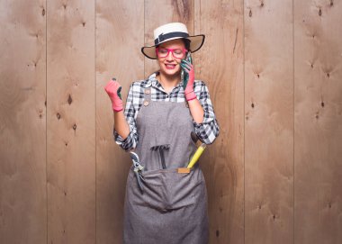 Heyecanlı genç bahçıvan kadın cep telefonuyla stüdyodaki ahşap arka planda yumruğunu tutuyor. Stüdyo çekimi