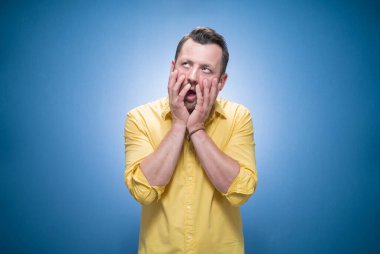 Sıkıcı adam uykulu ve isteksiz bakışlar atıyor, mavi arka planda sıkıcı bir konsept, sarı gömlek giyiyor. Stüdyo çekimi