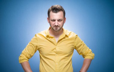 Mavi arka planda sana bakan, sarı gömlekli, otoriter bir adam. Kaşlarını çatmış, kıskanç bir adam. Stüdyo çekimi