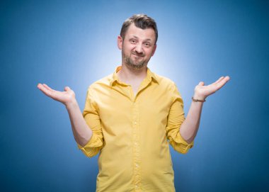 Beyaz arka plana karşı cahil genç adam karışık kolları açık mavi arka planda avuç içleri açık, sarı gömlekli. Stüdyo çekimi