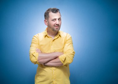 Kollarını mavi arka planda çapraz tutan, sarı gömlekli şüpheli ve tatminsiz bir adam. Kızgın ve sinirli yüz, şüpheci ve şüpheli ifade. Stüdyo çekimi