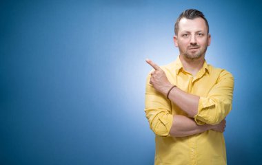 Sunum. Boşluğu işaret eden adam, fotokopi alanı, ürününüzü mavi arka planda sunan adam, sarı gömlekli adam. Tanıtımcı metnin için boşluk gösterir. Stüdyo çekimi