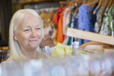 Senior Woman Buying Used Sustainable Clothes From Second Hand Charity Shop Or Thrift Store clipart