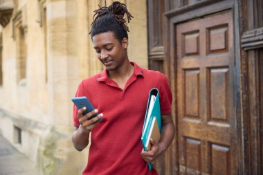 Oxford İngiltere 'deki üniversite binasının dışındaki cep telefonundan mesajları ya da sosyal medyayı kontrol eden erkek öğrenci