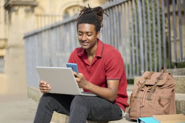 Oxford 'daki üniversite binasının dışındaki basamaklarda oturan erkek öğrenci laptopta mesajları veya cep telefonundaki sosyal medyayı kontrol ediyor.