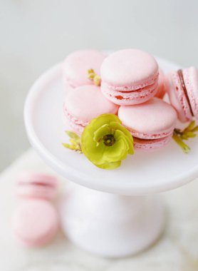 Pembe badem kurabiyeleri, yanında yeşil bir çiçekle birlikte beyaz bir pasta standında güzelce düzenlenir. Dekor, kutlamalar için mükemmel bir tatlı gösterisi yaratıyor..