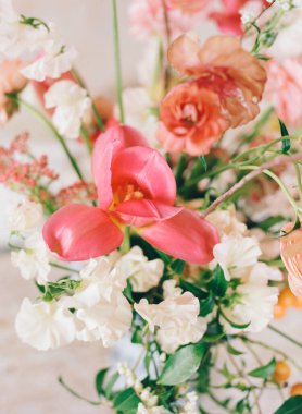 Canlı pembe laleler narin beyaz ve şeftali çiçeklerinin karışımı arasında göze çarpar. Düzenleme, bahar çiçeklerinin güzelliğini gözler önüne seren kırsal ahşap bir masanın üzerinde duruyor..