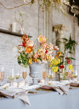 Göz kamaştırıcı bir çiçek süsü, ışıl ışıl gözlüklerle çevrili güller ve diğer çiçeklerle süslü, şık bir ortamda, bir etkinlik için mükemmel bir masa ayarları içerir..
