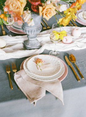 Güzel düzenlenmiş bir masa, bir vazoda narin güller ve renkli çiçekler, zarif tabaklar, bardaklar ve çatal bıçaklar, toplanma için mükemmel bir yemek atmosferi yaratıyor..