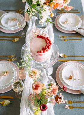 Çarpıcı bir tatlı masasında, zarif çiçek aranjmanları ve zarif sofra takımı ile çevrili taze ahudududularıyla süslenmiş, güneşli bir öğleden sonra kutlaması için mükemmel katmanlı bir pasta sergilenir..