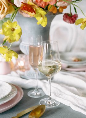 Güzel düzenlenmiş bir masa, canlı bir çiçek süsü, kabarcıklı içeceklerle dolu zarif bir cam süs ve yemek ve kutlama için neşeli bir atmosfer yaratan hassas bir bulaşık takımı içerir..