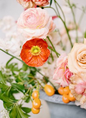 Göz kamaştırıcı bir çiçek aranjmanı yumuşak pastel güller ve parlak turuncu böğürtlenlerle vurgulanmış narin gelincikler sergiliyor, şık bir vazoda, her ortama neşe katıyor..