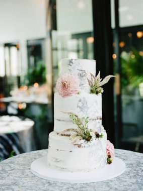 Zarif çiçekler ve yeşillik içeren üç katlı, kırsal bir don tasarımı olan çarpıcı bir düğün pastası. Zarif ortam, kutlama için mükemmel bir ortam yaratır..