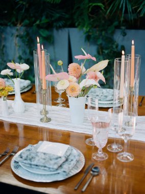 Güzel düzenlenmiş bir masa vazolarda taze çiçekler, zarif bir şekilde yerleştirilmiş tabaklar, kristal bardaklar ve yanan mumlar içerir. Davetkar bir açık hava akşam yemeği havası..