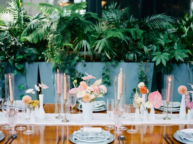 Güzel düzenlenmiş bir masa bir dizi taze çiçek ve zarif mumlar içerir. Canlı yeşilliklerle çevrili bu ortam, toplanma için sakin bir atmosfer yaratıyor..