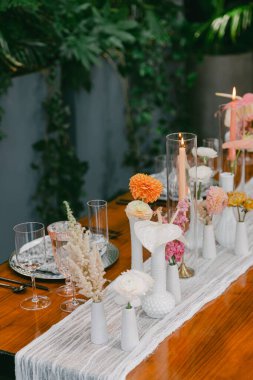 Güzel bir yemek masasında vazolarda bir dizi narin çiçek, mumlar yumuşak bir şekilde yakılır ve zarif bir cam eşyayla özel bir toplantı için sıcak bir atmosfer oluşturulur..