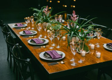 Güzel düzenlenmiş bir yemek masası lüks cam eşyalar, mor peçeteler ve zarif çiçekli süsler, sıcak ortam aydınlatmalı samimi bir gece toplantısı için hazırlanır..