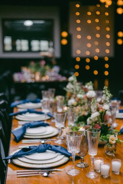 Güzel düzenlenmiş bir yemek masasında zarif çiçekli süsler, zarif cam süsler ve sıcak ışıklandırmalı sıcak bir mekanda özel bir toplantı için hazırlanmış yumuşak mavi peçeteler bulunur..