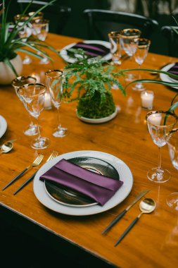 Çok güzel düzenlenmiş bir yemek masasında zarif cam eşyalar, şık çatal bıçaklar ve merkezi bir dekoratif bitki sergileniyor. Ortam, toplantı için mükemmel bir ortam olduğunu gösteriyor..