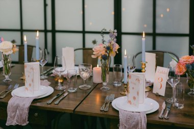 Zarif bir yemek masası zarif bir şekilde vazolarda narin çiçeklerin, mumların ve dikkatlice yerleştirilmiş sofra takımlarının bulunduğu özel bir toplantı için düzenlenir..