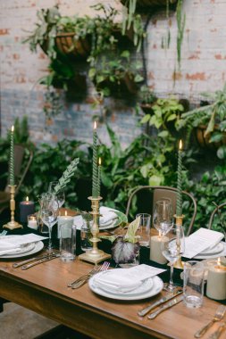 Çok güzel düzenlenmiş bir yemek masasında yeşil konik mumlar ve cam eşyalar, sıcak ve davetkar bir atmosferde canlı bitkilerle çevrili, toplanmak için mükemmel..