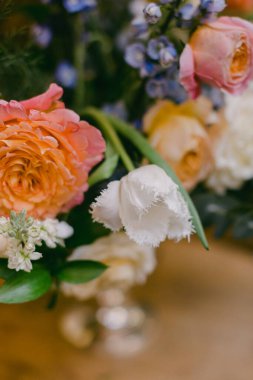 Renkli güller, laleler ve diğer çiçeklerden oluşan canlı bir karışım dekoratif bir vazoda sanatsal olarak düzenlenir. Kapalı ortamın havasını güzelleştirir. Kutlamalar için mükemmeldir..