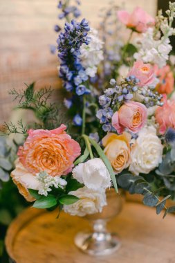 Göz kamaştırıcı pastel güller ve kır çiçeklerinden oluşan bir koleksiyon temiz bir vazoda canlı bir süs oluşturarak ahşap masanın kırsal cazibesini artırıyor. Bu düzenleme huzurlu bir ortam sunuyor..