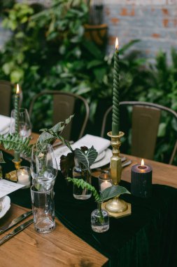 Zarif mumlar ve yemyeşil çiçeklerle dolu güzel bir yemek masası. Yumuşak parıltı sıcak bir atmosfer yaratıyor. Akşamları samimi bir toplantı için mükemmel..