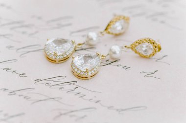 Delicate earrings with sparkling gems are artistically arranged on a piece of vintage handwritten paper. Soft lighting enhances the elegant details and charm of the jewelry. clipart