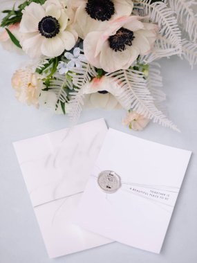 Deniz şakayıkları ve yumuşak yeşilliklerin yer aldığı bir buketin yanında güzel düğün davetiyeleri sergileniyor. Romantizm ve zarafetten oluşan bir zemin oluşturuyor..