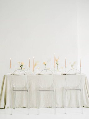 Güzel düzenlenmiş bir yemek masasında berrak sandalyeler ve yumuşak pastel çiçekler bulunur. Zarif mumlar, rafine atmosferi aydınlatan dik dururlar. Minimalist tasarım huzuru arttırır.