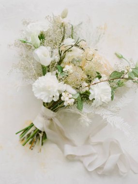 Beyaz çiçekleri ve yumuşak yeşilliği olan muhteşem bir düğün buketi. Kurdeleyle ustalıkla bağlanmış. Bu zarif parça gelin kutlamaları için mükemmel ve romantik estetiği yakalıyor..