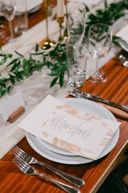 A beautifully arranged table with elegant place settings, greenery accents, and a menu card for a festive gathering. clipart