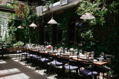 Yeşillik ve doğal ışıkla çevrili, akşam yemeği için hazırlanmış uzun ahşap masa gün boyunca akıyor..