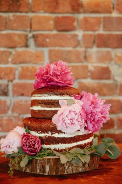 Pembe çiçeklerle süslenmiş üç katlı bir pasta kırsal bir duvarın önündeki tahta bir levhaya konur..