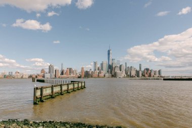 Ufuk çizgisi, suyun yanında modern binalar ve mavi gökyüzünün altında nehre uzanan bir rıhtıma sahiptir..