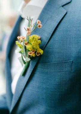Damat zarif bir çiçek ve yeşillik yaka çiçeğiyle kutlamada mavi takımını eşleştiriyor..