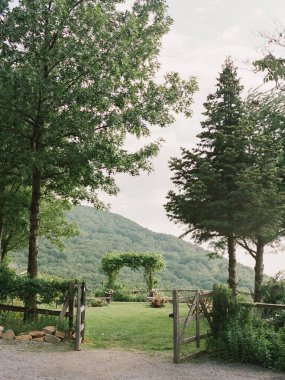 Ziyaretçiler, canlı ağaçlar ve manzaralı bir dağ zeminiyle çevrili sakin bir bahçe girişi tarafından karşılanıyor..