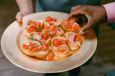 Bir el sosyete toplantısında altın tepside taze domates ve otlarla kaplı bruschetta 'ya uzanır..
