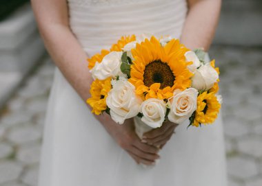 Gelin, canlı ayçiçeği buketini ve beyaz güllerini bir bahçede düğün töreninde sergiliyor..
