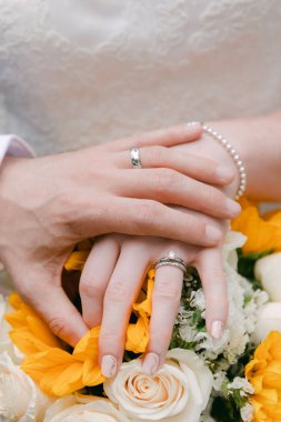 Bir çift, neşe dolu bir düğün töreninde çiçek aranjmanının üstünde alyanslarını gösteriyor..