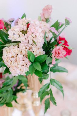 Taze pembe ve beyaz çiçekler sanatsal olarak altın bir vazoda düzenlenir ve şenlikli atmosfere zarafet katar..