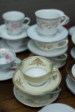 Hassas bir çay fincanı koleksiyonu ve çay fincanları ahşap bir masaya güzelce istiflenmiş, karmaşık çiçek desenleri sergiliyor. Sıcak atmosfer gevşemeyi ve konuşmayı davet eder..