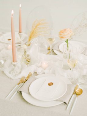 Güzel düzenlenmiş bir masa, pembe mumları, narin çiçekleri ve zarif yemek takımlarıyla yumuşak pastel renklere sahiptir. Kutlama için sıcak bir atmosfer yaratırlar..