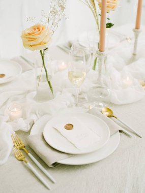 Güzel düzenlenmiş bir yemek masasında beyaz bir masa örtüsü, zarif bir cam eşyalar, yumuşak mumlar ve taze güller bulunur. Sıcak mum ışığı misafirler için romantik bir ortam yaratır..