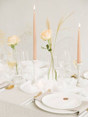 Güzel düzenlenmiş bir masa uzun mumlar ve vazolarda narin güller içerir. Romantik bir akşam yemeği için davetkar bir ortam yaratır. Yumuşak ışıklandırma zarafeti artırır.