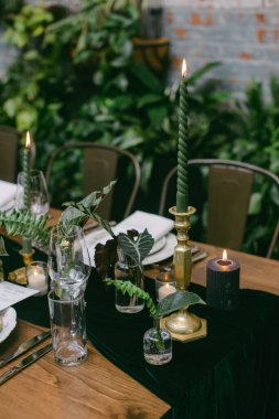 Zarif mumlar ve yemyeşil çiçeklerle dolu güzel bir yemek masası. Yumuşak parıltı sıcak bir atmosfer yaratıyor. Akşamları samimi bir toplantı için mükemmel..