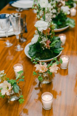 Güzel düzenlenmiş bir masa, zarif çiçek süslemeleri ve yumuşak mum ışığı içerir. Bir toplantı ya da kutlama için sıcak bir atmosfer yaratır. Misafirler davet ortamının tadını çıkarıyorlar..